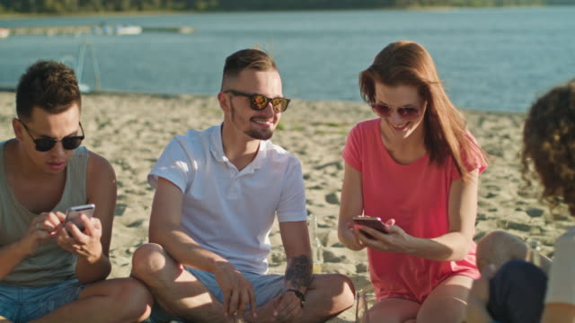 Jóvenes-divirtiéndose-en-la-playa-utilizando-teléfonos