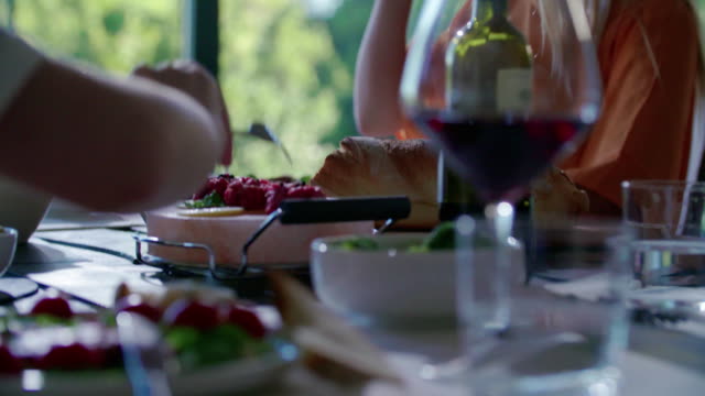 People-eating.Four-caucasian-friends-man-and-woman-mediterranean-italian-salad,meat-steak-and-bread-lunch-or-dinner.-Summer-party-at-home-in-modern-house-4k-handheld-video