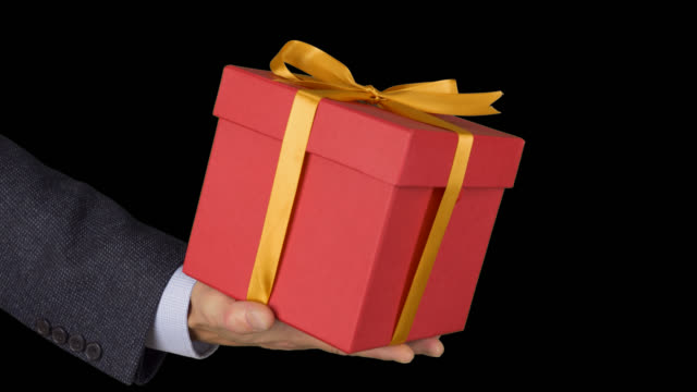 Male-man-hand-holds-red-gift-box-with-gold-bow.-Celebrate-eve-present-gift-box.-Caucasian-man-in-classical-suit.-Alpha-channel-chroma-key-transparent-background.-Locked-down.