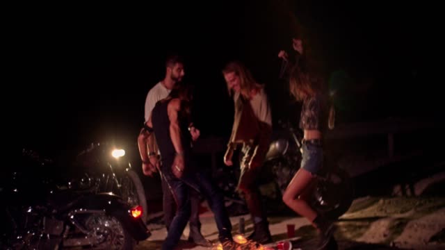 Young-drunk-rebel-friends-with-motorcycles-dancing-around-campfire
