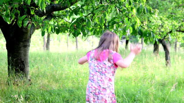 Eine-niedliche-Mädchen-tanzt-in-den-Naturgarten.-Kleine-Mädchen-tanzt-und-springt-auf-einem-kleinen-Trampolin.-Kleines-Mädchen-trägt-geblümten-Kleid-und-weißen-Hut