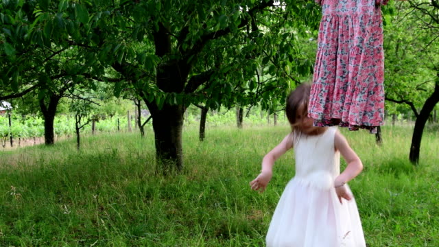 A-cute-girl-dances-in-the-natural-garden.-Little-girl-dances-and-jumps-on-a-small-trampoline.-Little-girl-wears-white-wedding-dress