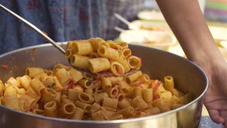 Young-happy-kids-preparing-eating-lunch-pasta-in-summer-camp-outside-on-sunny-day-in-park-serving-food-from-pot-pan-slow-motion