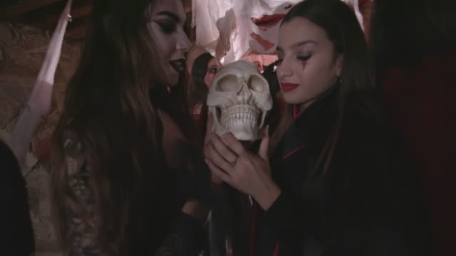 Mujeres-jóvenes-en-trajes-miedosas-lamiendo-cráneo-en-fiesta-de-Halloween
