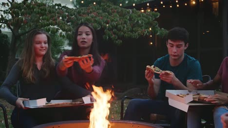 Amigos-adolescentes-se-sientan-alrededor-de-una-hoguera-comiendo-pizzas-para-llevar