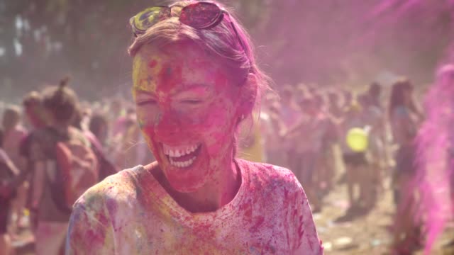 Young-happy-girl-in-colourful-powder-is-histerically-laughing-and-dancing-on-holi-festival-in-daytime-in-summer,-watching-at-camera,-color-concept,-emotional-concept
