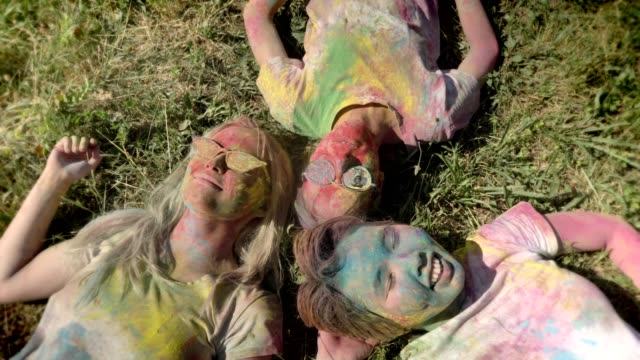 Three-young-happy-multi-ethnic-girlfriends-are-laying-on-grass-on-holi-festival-in-daytime-in-summer,-friendship-concept,-holiday-concept