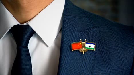 Businessman-Walking-Towards-Camera-With-Friend-Country-Flags-Pin-China---Lesotho