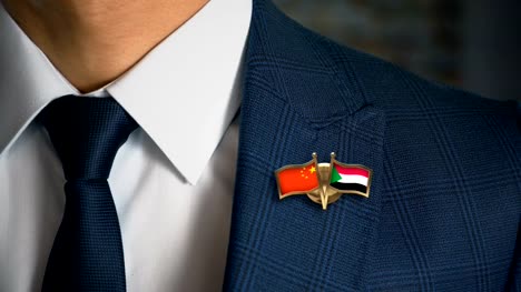 Businessman-Walking-Towards-Camera-With-Friend-Country-Flags-Pin-China---Sudan