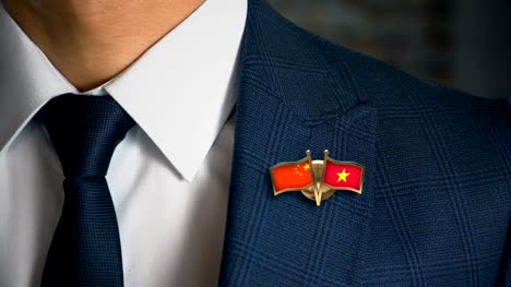 Empresario-caminando-hacia-cámara-con-amigo-país-banderas-Pin-China---Vietnam