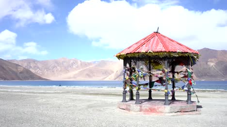 Roter-Pavillon-in-Bergen-und-Pangong-Tso-(See)-und-Gebetsfahnen-flattern-im-Wind.-Es-ist-riesig-und-höchste-See-in-Ladakh-und-blauer-Himmel-im-Hintergrund,-es-erstreckt-sich-von-Indien-nach-Tibet.-Leh,-Ladakh