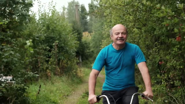 Senior-kaukasischen-Männchen-im-blauen-T-shirt-seinen-Sommer-Urlaub-mit-dem-Fahrrad-zwischen-den-Bäumen-im-Freien-zu-genießen.