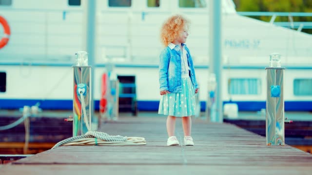 Small-and-beautiful-red-haired-child-girl-walks-by-the-pier-for-boats-and-yachts