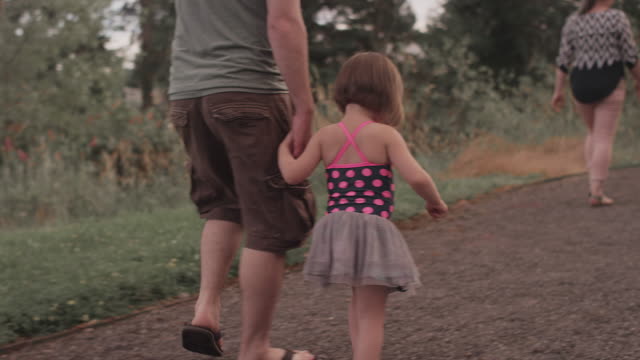 A-little-girl-and-her-dad-walk-hand-in-hand-down-a-park-trail