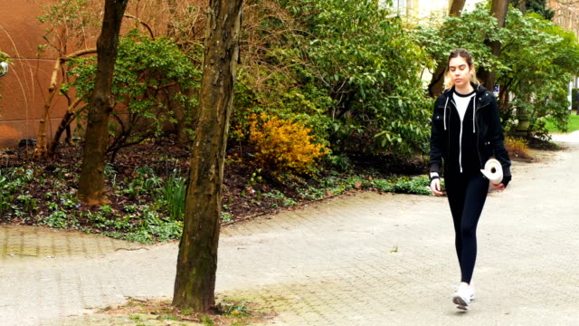 Mujer-caminando-con-estera-del-ejercicio-en-el-Parque-4k