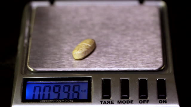 Electronic-scales-with-tablet-on-black-background.-Laboratory-scales.-Pills-and-medication-health,-close-up.-Gray-pills-on-electronic-scales