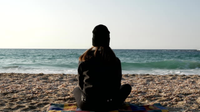 Mädchen-sitzt-auf-dem-Strand-des-Mittelmeers-an-einem-kühlen-Herbsttag.