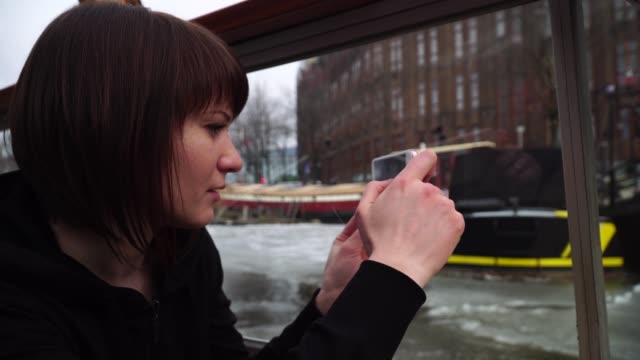 Frau-Segel-auf-einem-Boot-durch-die-Grachten-in-Amsterdam-und-nimmt-Bilder-auf-dem-Handy
