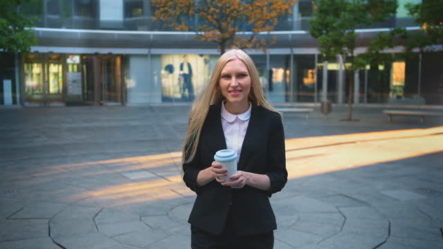 Formal-woman-drinking-coffee-in-patio.-Elegant-blond-woman-in-suit-and-with-long-hair-drinking-coffee-from-white-cup-in-patio-with-trees