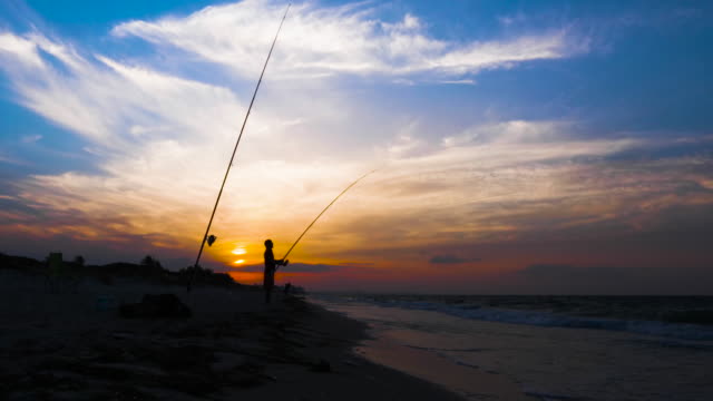 Männliche-Fisher-ziehende-Fische-mit-Angelrolle-und-Stab-aus-Meer,-silhouette