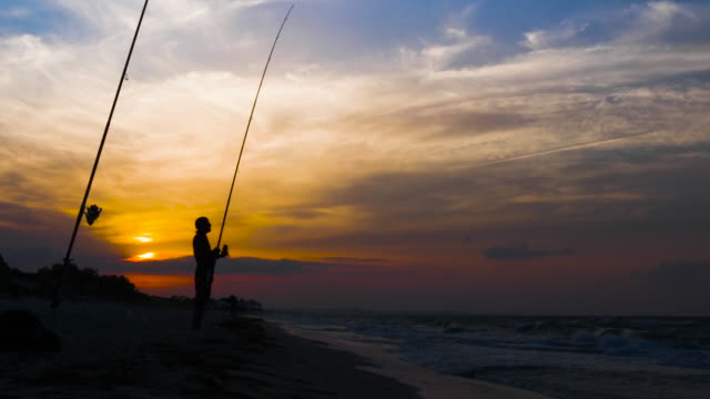 Allein-Fischer-dreht-Angelrolle-Angelrute,-Silhouette-auf-Meer-Sonnenuntergang