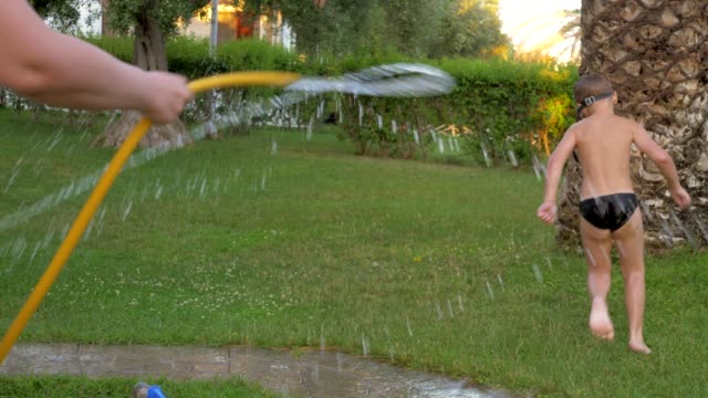 Child-running-away-from-mother-washing-him-from-the-hose-outdoor