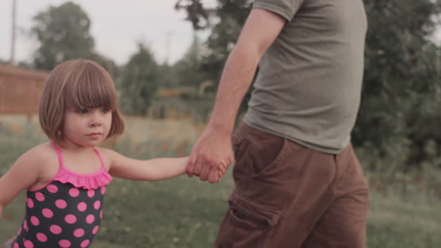 A-little-girl-and-her-dad-walk-hand-in-hand-down-a-park-trail