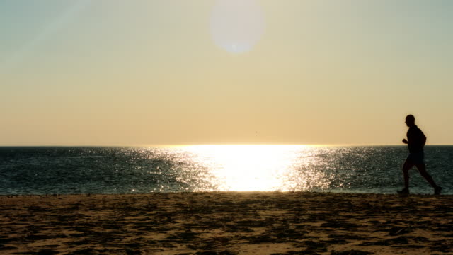 male-runner-running-on-beach,-sunset-silhouette,-slow-motion