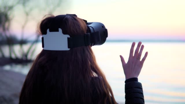 Atractiva-mujer-blanca-está-utilizando-gafas-de-realidad-virtual-por-el-lago-al-atardecer