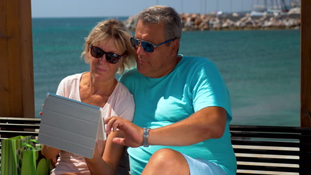 Senior-couple-using-touch-pad-on-waterfront