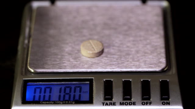 Electronic-scales-with-tablet-on-black-background.-Laboratory-scales.-Pills-and-medication-health,-close-up.-Gray-pills-on-electronic-scales