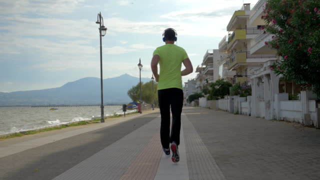 Junger-Mann-im-Kopfhörer-läuft-auf-Straße-der-Stadt-Perea,-Griechenland
