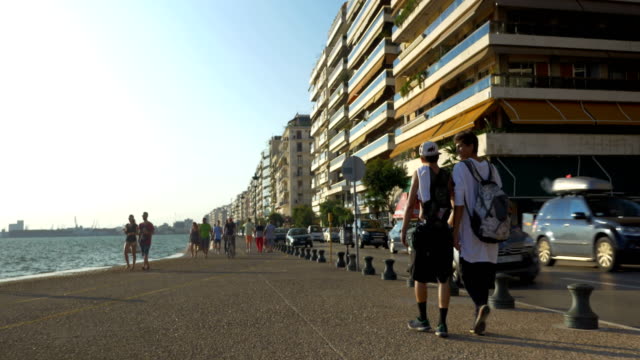 Two-young-boys-walk-along-the-seafront-of-Thessaloniki,-Greece