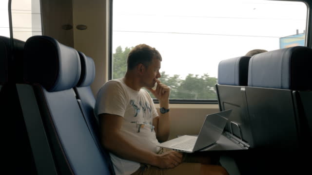 View-of-young-man-riding-in-the-train-and-working-with-laptop-on-the-table-against-window,-Netherlands