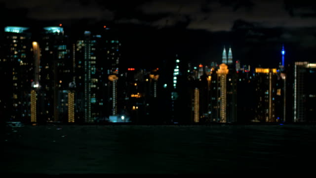 View-of-woman-swimming-in-the-pool-on-the-skyscraper-roof-against-night-city-landscape.-Kuala-Lumpur,-Malaysia