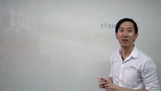 Young-Asian-foreign-oriental-language-instructor-giving-a-language-lesson-in-classroom---Asian-language-education-concept-such-as-Japanese,-Korean,-Chinese----Characters-on-the-board-are-Chinese-and-Hello-in-Chinese