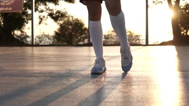 Junges-Mädchen-ihre-Beine-in-weißen-Turnschuhen-und-weißen-Golfsocken-auf-dem-lokalen-Basketball-Platz.-Nicht-erkennbare-Footage-mit-Sonne-auf-dem-Hintergrund