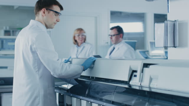 Research-Scientist-Puts-Test-Tubes-with-Blood-Samples-Into-Analyzing-Machine.-Innovative-Pharmaceutical-Lab-with-Modern-Medical-Equipment-Doing-Genetics-Research.