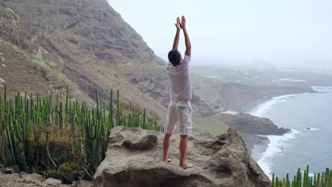 Fit-young-man-practices-sun-salutation-yoga-in-mountain-for-ocean.-Young-man-enjoying-meditation-and-yoga.-fitness,-sport,-people-and-lifestyle-concept---young-man-making-yoga-exercises