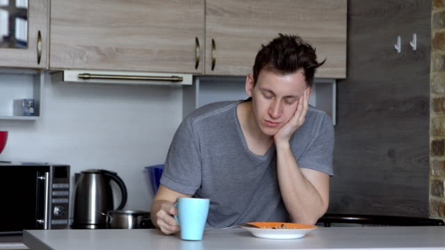 Man,-falling-asleep,-eats-oatmeal-and-coffee-in-the-kitchen
