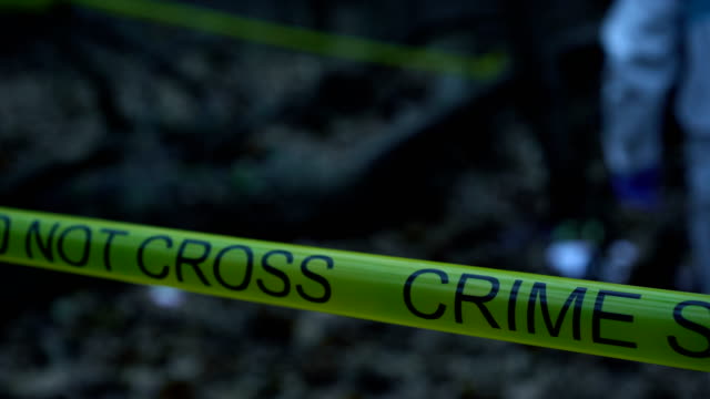 Closeup-of-yellow-crime-scene-tape-in-the-woods,-forensic-expert-working-at-site