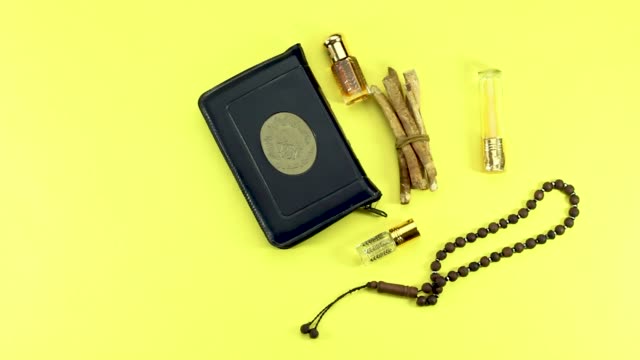 Frau-Hand-setzen-heiliges-Buch-der-Muslime-und-Rosenkranz,-Siwak,-Parfüm-auf-gelbem-Hintergrund