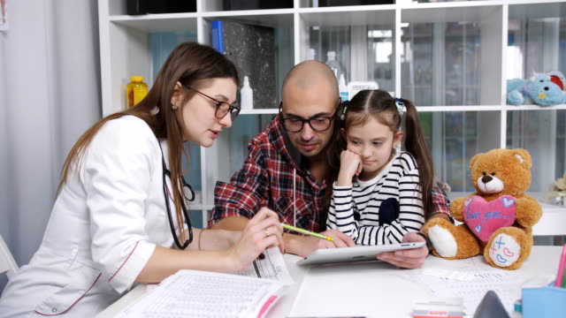 Arzt-zeigt-auf-dem-Tablett-an-dem-Vater-mit-der-kleinen-Tochter-eine-Anwendung-für-Gesundheitskontrolle