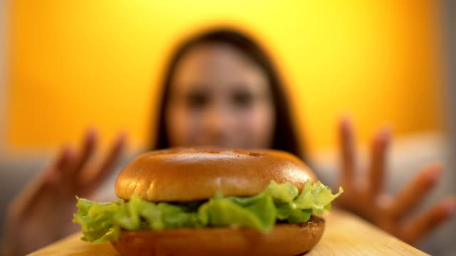 Persona-sirve-hamburguesa-a-niña-hambrienta,-mujer-comiendo-con-apetito-y-avaricia