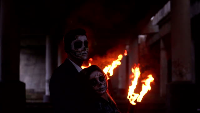 Ehepaar-mit-Schädel-Make-up-auf-dem-Hintergrund-von-brennendem-Feuer-und-Rauch.-Halloween