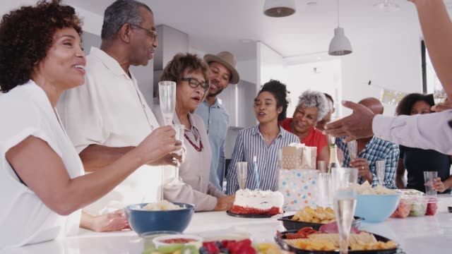 Obere-schwarze-Frau,-die-die-Kerze-auf-Geburtstagstorte-während-einer-Feier-mit-ihrer-Familie-ausblasen