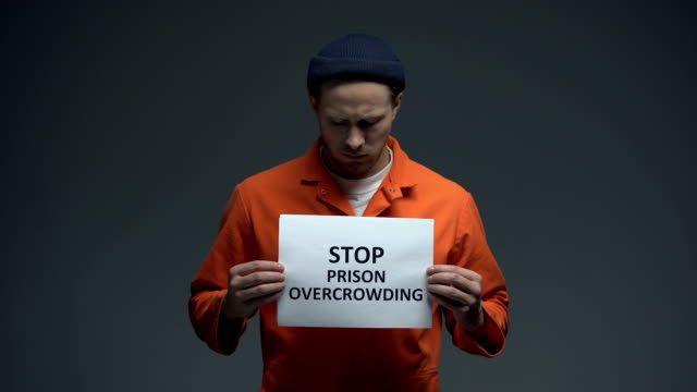 Prisoner-holding-Stop-prison-overcrowding-sign-in-cell,-life-conditions-in-jails