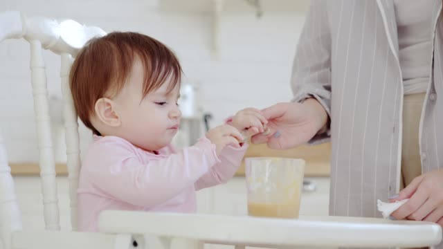 Cute-baby-girl-refusing-to-eat-fruit-puree,-but-her-patient-mother-managing-to-feed-her-with-spoon