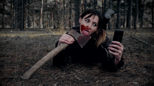 Frau-mit-blutigem-Make-up-macht-lustige-Selfies-auf-Handy-für-soziale-Netzwerke-an-Halloween-im-Wald
