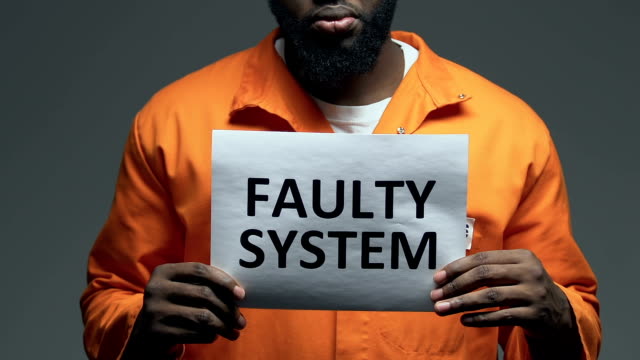 Faulty-system-phrase-on-cardboard-in-hands-of-Afro-American-prisoner,-disorder